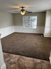 Empty room featuring wainscoting, a ceiling fan, dark colored carpet, and a textured ceiling