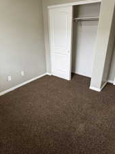 Unfurnished bedroom featuring baseboards, dark carpet, and a closet