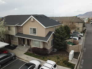 View of front of property with stucco siding, uncovered parking, and a shingled roof