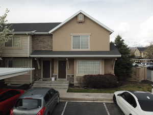 View of front of property featuring a shingled roof, uncovered parking, stucco siding, and stone siding