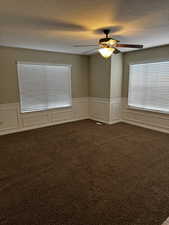 Spare room featuring wainscoting, a textured ceiling, dark colored carpet, and ceiling fan