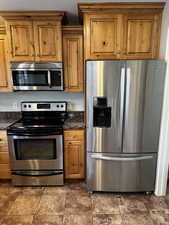 Kitchen with dark stone countertops, stainless steel appliances, and brown cabinetry