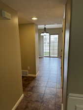 Hallway featuring a notable chandelier, a textured ceiling, baseboards, visible vents, and dark tile patterned flooring