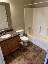 Bathroom featuring toilet, stone finish flooring, vanity, tub / shower combination, and a textured wall