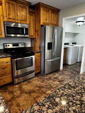 Kitchen featuring washing machine and clothes dryer, appliances with stainless steel finishes, brown cabinetry, and a textured ceiling