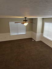 Spare room featuring a ceiling fan, a textured ceiling, dark carpet, and wainscoting