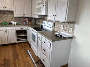 Kitchen with white appliances, white cabinetry, tasteful backsplash, and dark wood-style flooring