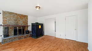 Unfurnished living room featuring a stone fireplace, baseboards, and wood finished floors