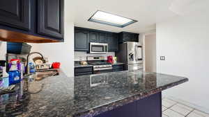 Kitchen featuring light tile patterned floors, stainless steel appliances, dark stone countertops, a sink, and a peninsula