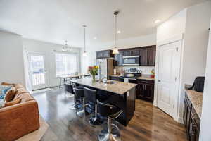 Kitchen with stainless steel appliances, dark wood-type flooring, dark brown cabinetry, a sink, and a breakfast bar area