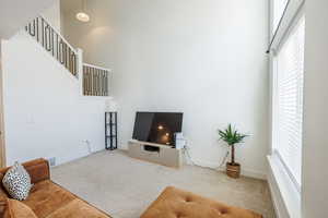Carpeted living room with a high ceiling, baseboards, stairs, and visible vents