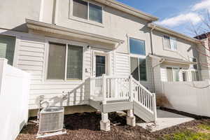 View of exterior entry featuring cooling unit, stucco siding, and fence