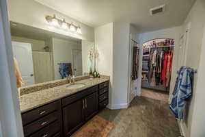 Bathroom featuring a textured ceiling, visible vents, a shower, vanity, and a spacious closet
