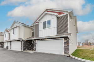 View of front of home featuring driveway, an attached garage, stone siding, and board and batten siding