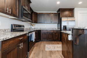 Kitchen featuring dark brown cabinets, light stone counters, light wood-style floors, and appliances with stainless steel finishes