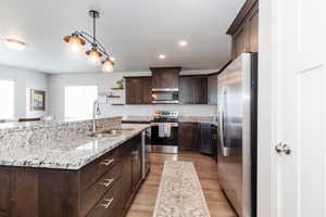 Kitchen featuring a center island with sink, dark brown cabinets, a sink, and stainless steel appliances