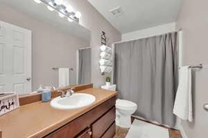Bathroom with curtained shower, visible vents, toilet, and vanity