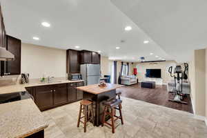 Kitchen featuring a sink, freestanding refrigerator, stainless steel microwave, recessed lighting, and dark brown cabinets
