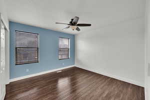 Unfurnished room with dark wood-style floors, baseboards, and a ceiling fan