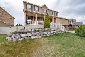 View of front of house with stucco siding, fence, driveway, a front lawn, and covered porch