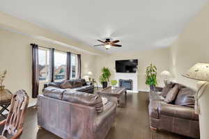 Living area featuring dark wood-type flooring, baseboards, ceiling fan, and a glass covered fireplace