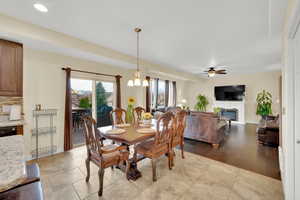 Dining space with ceiling fan with notable chandelier, stone tile flooring, baseboards, and a glass covered fireplace
