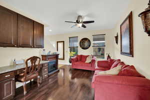 Living room featuring dark wood-type flooring, baseboards, built in desk, ceiling fan, and recessed lighting