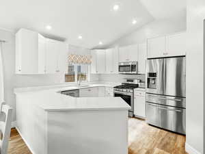 Kitchen with a peninsula, appliances with stainless steel finishes, white cabinetry, a sink, and light wood-style floors