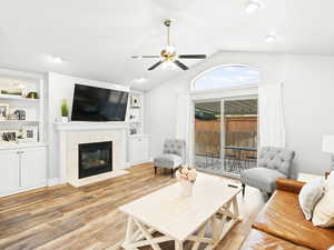 Living area with lofted ceiling, light wood-style flooring, a ceiling fan, a tile fireplace, and built in features