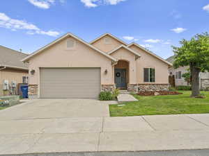 View of front of house featuring a front yard, stone siding, concrete driveway, stucco siding, and an attached garage