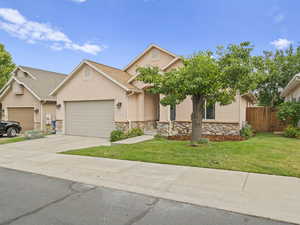 View of front of house featuring stucco siding, an attached garage, stone siding, driveway, and a front lawn
