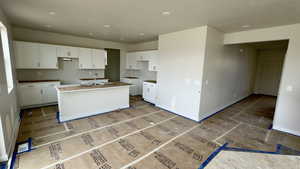 Kitchen featuring white cabinetry, baseboards, and an island with sink