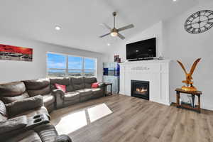 Living room featuring light wood finished floors, ceiling fan, recessed lighting, lofted ceiling, and a glass covered fireplace