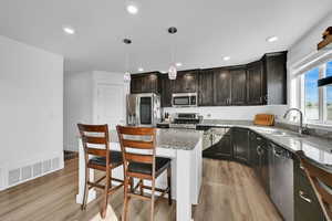 Kitchen featuring visible vents, light wood finished floors, stainless steel appliances, a sink, and light stone counters