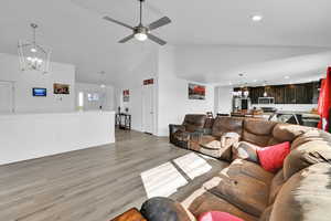 Living room with recessed lighting, light wood-type flooring, high vaulted ceiling, ceiling fan with notable chandelier, and baseboards