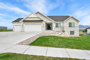 Craftsman house with board and batten siding, stone siding, an attached garage, a front yard, and driveway