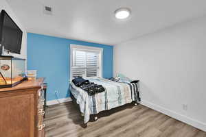 Bedroom with wood finished floors, baseboards, and visible vents