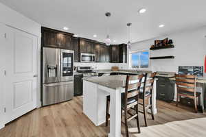 Kitchen with a breakfast bar area, light stone counters, light wood-type flooring, and appliances with stainless steel finishes