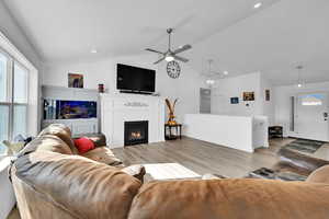 Living room featuring a ceiling fan, a warm lit fireplace, light wood-type flooring, lofted ceiling, and recessed lighting