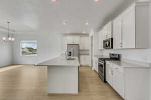 Kitchen with white cabinetry, an inviting chandelier, stainless steel appliances, a textured ceiling, and light wood finished floors