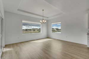 Spare room with baseboards, an inviting chandelier, light wood-type flooring, and a raised ceiling