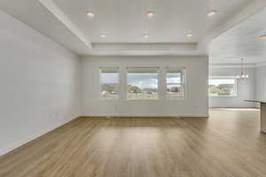 Unfurnished living room with light wood-style flooring, baseboards, a chandelier, and a raised ceiling