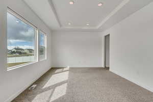 Empty room featuring carpet floors, a raised ceiling, baseboards, visible vents, and recessed lighting