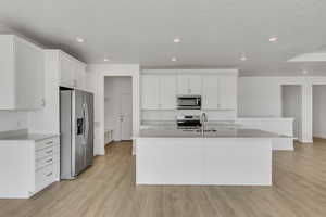Kitchen with white cabinets, stainless steel appliances, a center island with sink, a sink, and light wood-style floors
