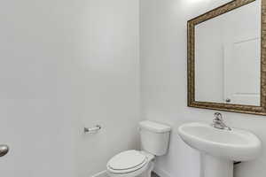 Half bath featuring baseboards, toilet, and a sink
