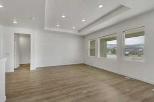 Unfurnished room featuring baseboards, wood finished floors, recessed lighting, and a raised ceiling