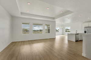 Unfurnished living room featuring light wood-style flooring, a sink, a tray ceiling, and a chandelier