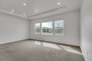 Carpeted empty room featuring baseboards, recessed lighting, and a raised ceiling
