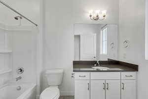 Bathroom featuring toilet, vanity, shower / bathing tub combination, and baseboards