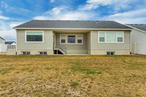 Back of house with roof with shingles, stucco siding, fence, and a lawn